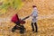 Mom walks in autumn Park with baby Stroller. Mother and child in autumn forest