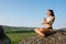 Moment of full relax and harmony. Pretty brunette woman in sporrtswear practicing yoga on the rock. Green mountain