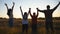 Mommy and daddy with two small children stand on grass field with raising hands at sunset. Happy young family enjoy to