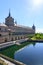 Monastery of El Escorial with water pond, gardens and flashes of sun in the blue sky.