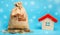 Money bag with coins and a wooden house with snow. Real estate market in the winter season. Christmas sale / discounts concept.