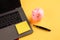 Moneybox near laptop and yellow sticky note, place for text. Finance and budget concept. Piggy bank in pink color with