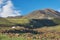 Mongolian landscape with mountain steppe under running cumulus clouds on blue sky, yurts and goats herd