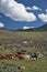 Mongolian landscape with mountain steppe under running cumulus clouds on blue sky, yurts and goats herd