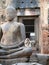 Monkey eating a piece of corn-on-the cob sitting on a Buddha statue at historic Wat Phra Phang San Yot