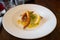Monkfish with monkfish scampi on a bed of saffron and pesto risotto and a lemon garnish in a white dish on a wooden table