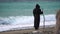 Monks wearing black robes walks on the beach with woden stick in hands at morning. Unrecognizable persone, slow motion.