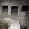 Monochrome image of a dark underground tomb with stone bridge connecting burial chambers in paphos cyprus