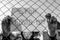 Monochrome image of a desperate teenage boy wearing surgical mask holding a message  behind a wired fence in isolation