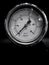 Monochrome image of a round pressure meter with a numbered dial on a dark background