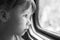 Monochrome portrait of a beautiful girl who looks in the window of the train. Close-up of a sad child looking through window. Blac