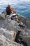 Montenegro, Budva - July 14, 2018: Fisherman fishing in the sea on the stone shore, and three cats waiting to catch