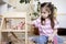 Montessori material. Child girl in pink T-shirt arranges wooden furniture in a doll house