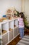 Montessori material. Child girl in pink T-shirt arranges wooden furniture in a doll house