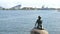 Monument of little mermaid in background of modern cityscape of Copenhagen in sunny day
