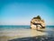 Monument rock in shallow sea waters. One big boulder with trees and plants laying on sand in turquoise sea. Travel