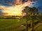 Moody autumnal farmland countryside landscape with tress,fields, hay bale under a clouded sunny sky