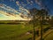 Moody autumnal farmland countryside landscape with tress,fields, hay bale under a clouded sunny sky