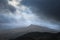 Moody and dramatic Winter landscape image of Moel Saibod from Crimpiau in Snowdonia with stunning shafts of light in stormy