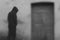 A moody dream like concept of a dark hooded figure standing next to an old wooden door. With an abstract blurred edit