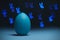 Moody easter concept in classic blue color. Blue cyan colored egg on black background with bunny shaped bokeh. Selective focus.