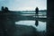 A moody figure, reflected in a puddle. Standing under a bridge in a post industrial landscape. With a grunge, abstract, edit