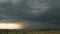 Moody landscape with dark stormy clouds with falling heavy downpour shower rain over distant town buildings in summer.