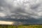 Moody landscape with dark stormy clouds with falling heavy downpour shower rain over distant town buildings in summer