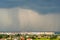 Moody landscape with dark stormy clouds with falling heavy downpour shower rain over distant town buildings in summer