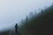 A moody lone hooded figure, back to camera standing on a path Looking at a foggy hillside on a moody atmospheric day