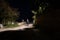 A moody night scene of a hooded man standing on a country lane lit up with a street light on a summers night