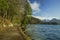 Moody pine forest peaceful landscape narrow ground trail along lake coast line with north mountains snowy peak background nature