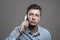 Moody portrait of confident young stubble man in blue shirt talking on the cellphone