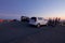 The moon glows above parked cars and people viewing the city of Victoria, BC, from the top of Mount Tolmie at sunset