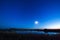 The moon and the stars in the night sky reflected in the river.