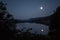 Moonlight from a glowing fullmoon reflected in a lake at midnight with mountains and trees around