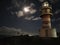 Moonlit path on the ocean and a beautiful large lighthouse on the rocky coast.  Night lighthouse