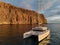 Moored lonely modern catamaran in calm waters of Atlantic Ocean near rocky volcanic cliff