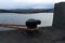 A mooring post on a river pier with a white-red rope.