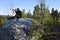 Moose hunter sitting on a big stone aiming with a rifle