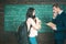 More knowledge. Woman student in glasses with book stack and backpack stand with teacher man on chalkboard in classroom