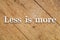 `Less is more` white text on a wooden background.