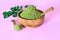 Moringa powder in wooden bowl with original fresh Moringa leaves on pink background