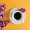 Morning coffee in a white cup with fragrant lilac flowers on a yellow cheerful background. Aroma concept, good morning.