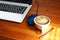 Morning coffee on worker table . light and shadow on white coffee cup on wood floor with blur laptop background