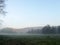 Morning fog on meadow with trees and hills with forest silhouettes