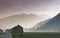 Morning mist in a mountain valley with fields and old wooden barns and lattice cross power lines and mountains in silhouette behin