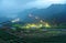 Morning scenery of tea gardens in the deep blue twilight before dawn with beautiful lights from the village in the valley