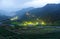 Morning scenery of tea gardens in the deep blue twilight before dawn with beautiful lights from the village in the valley