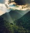 Morning sun rays coming through clouds and falling on green vegetation on mountain.